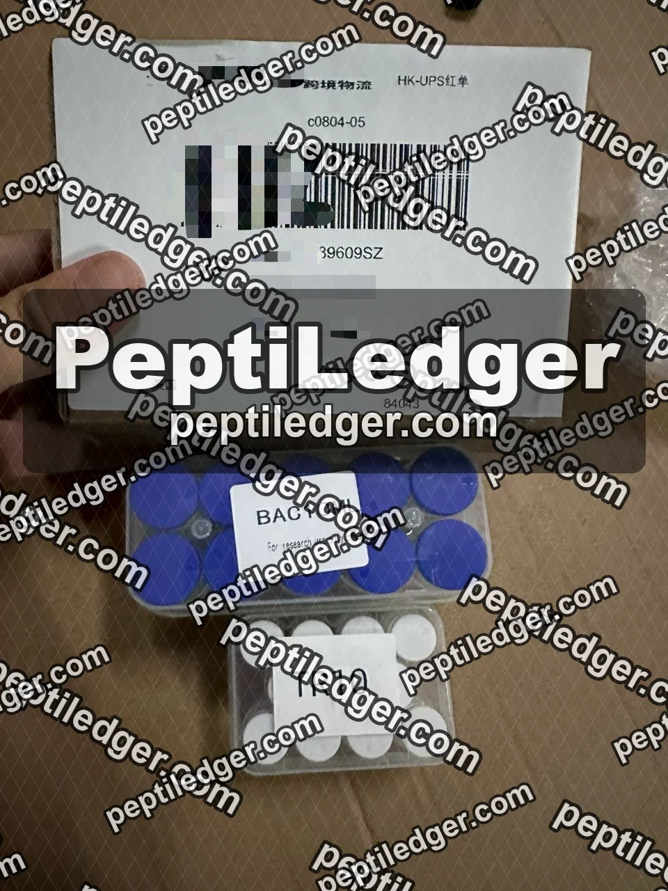 A hand holding a courier label with a tracking barcode above two boxes of vials with white lid labels.